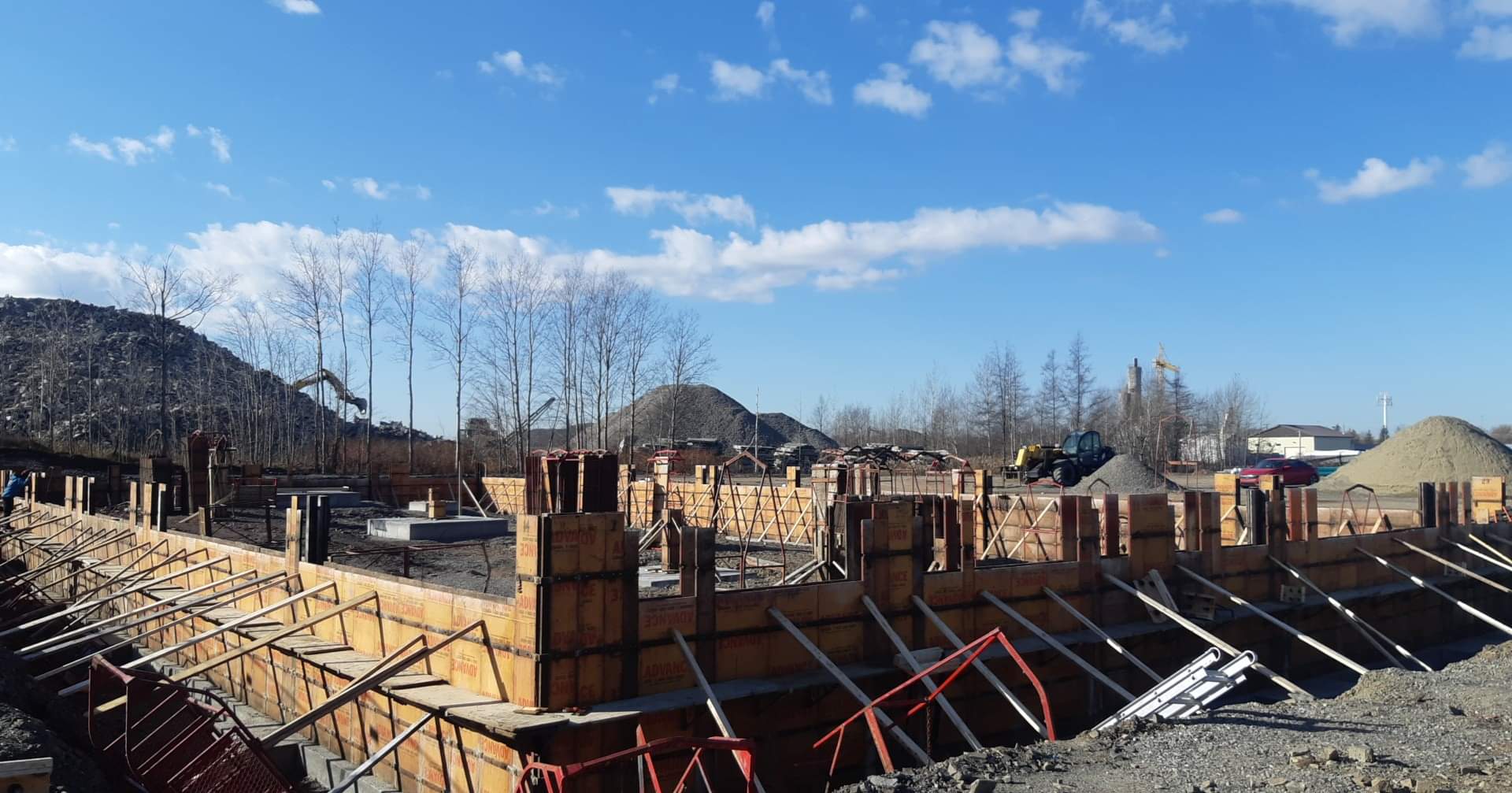 Un chantier de construction avec un ciel bleu et des arbres en arrière-plan.