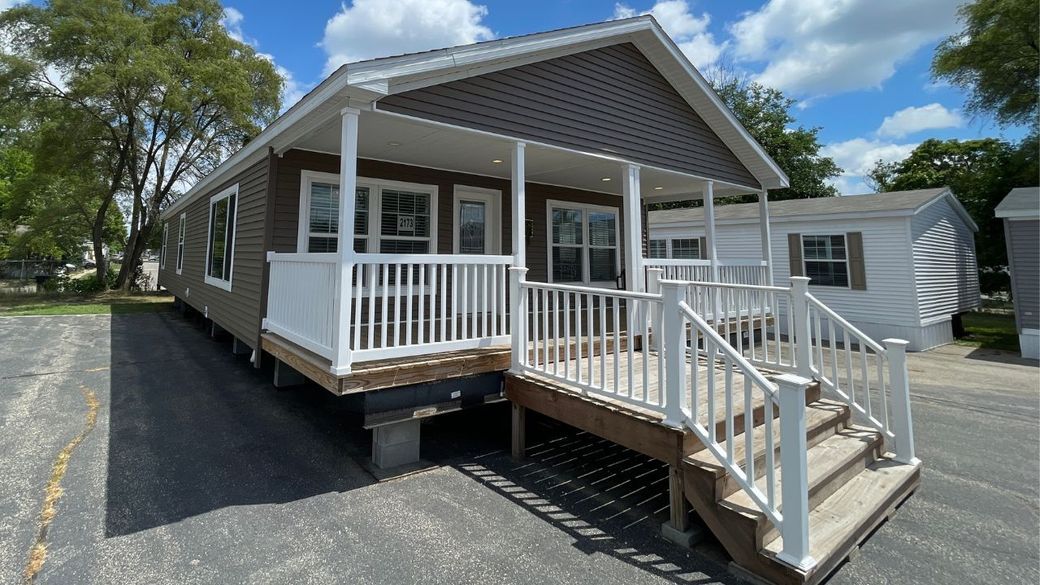 A small brown and white house with a porch and deck on a sunny day.