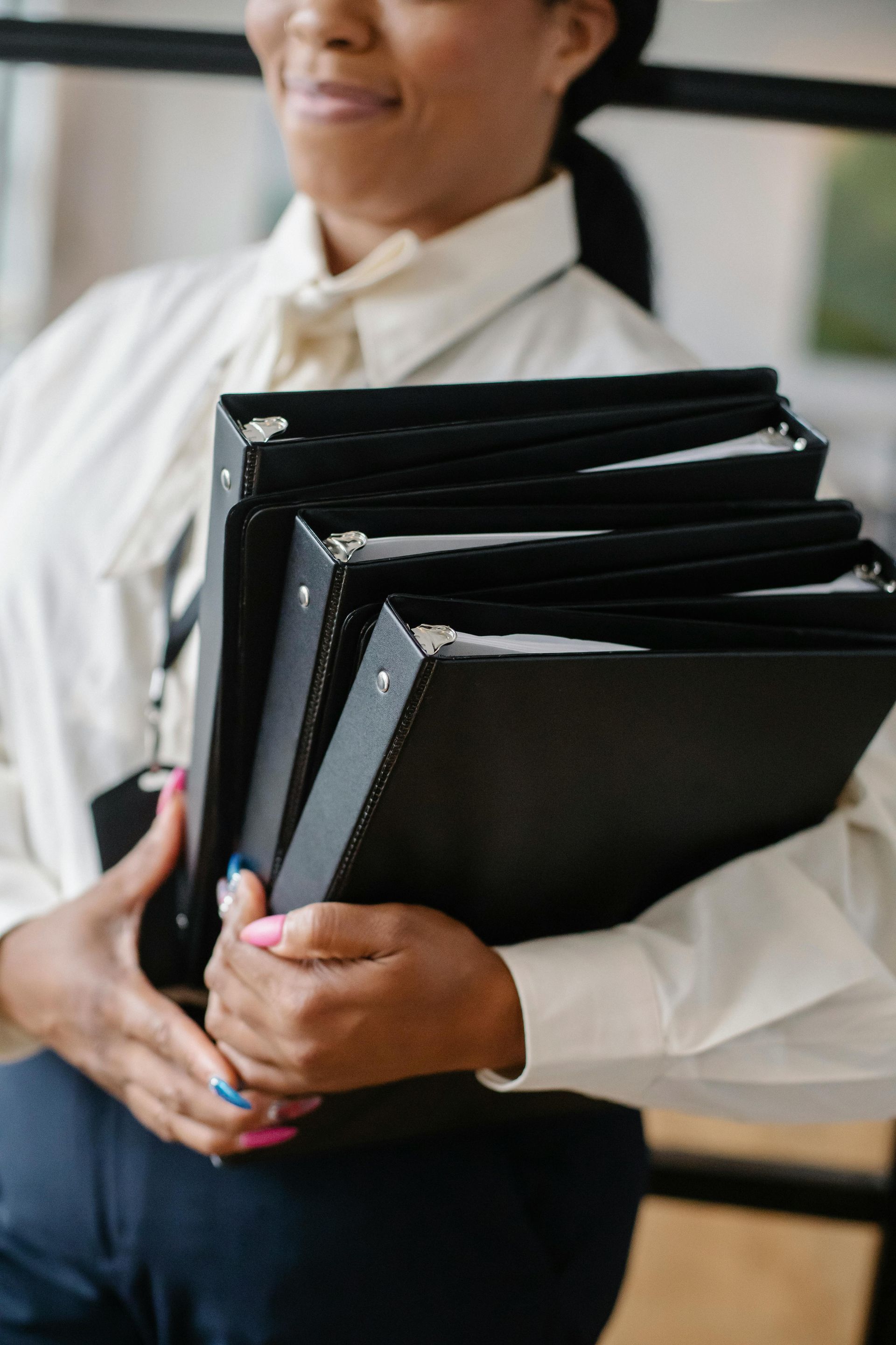 A woman is holding a stack of black binders in her hands.