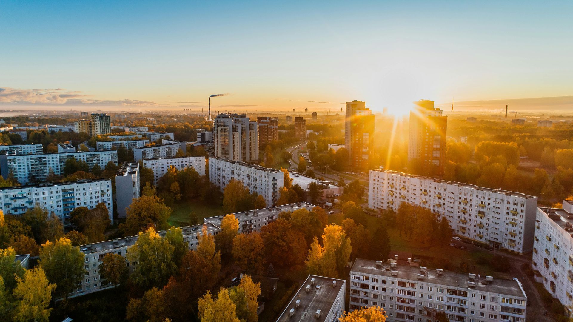 An aerial view of a city at sunset with the sun shining through the buildings.