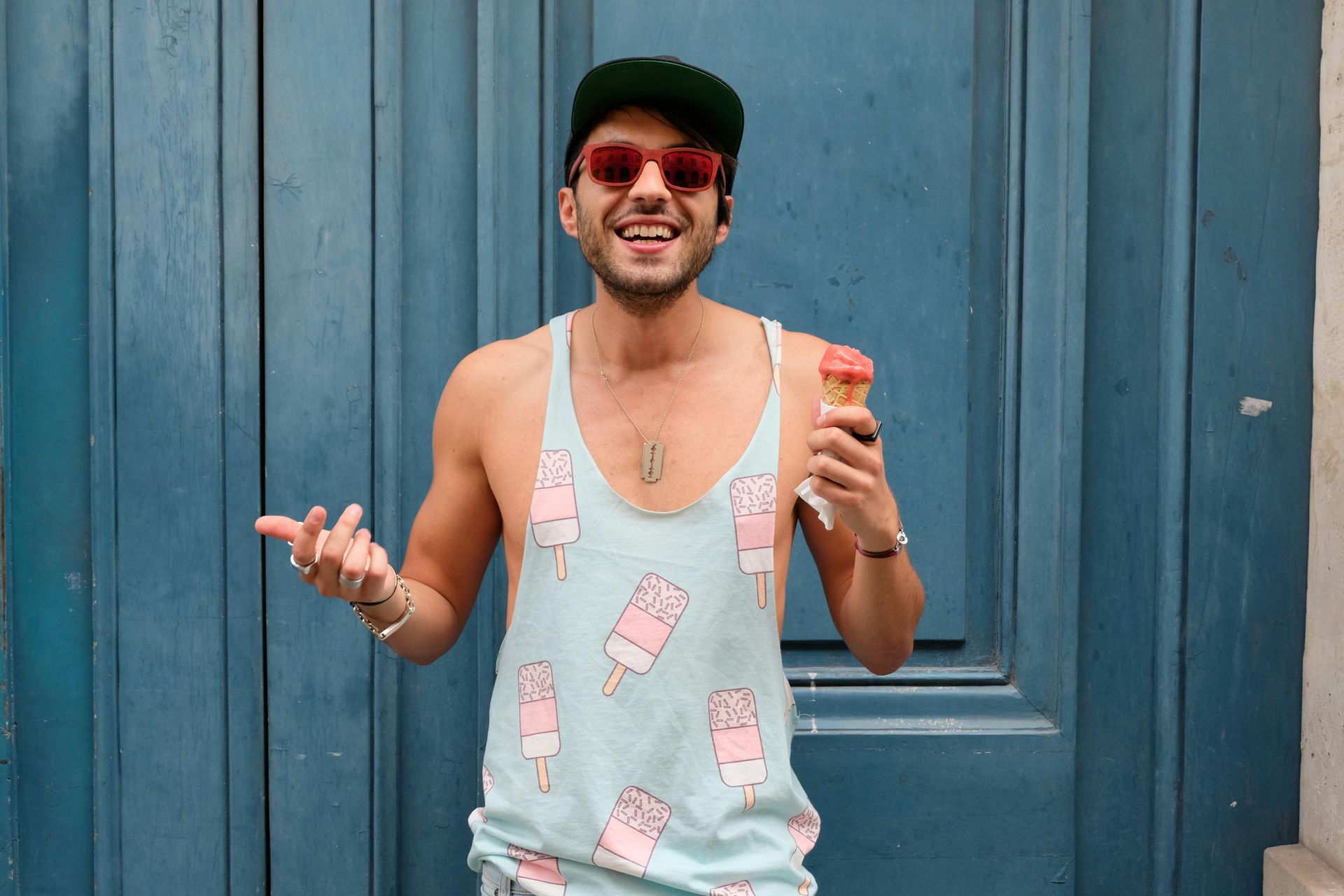 A man wearing sunglasses and a tank top is holding an ice cream cone.