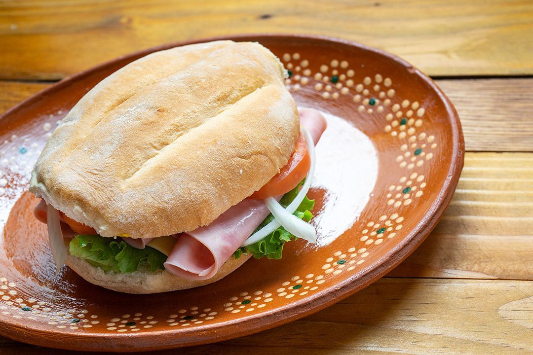 Un sándwich con jamón, lechuga, tomates y cebollas en un plato sobre una mesa de madera.