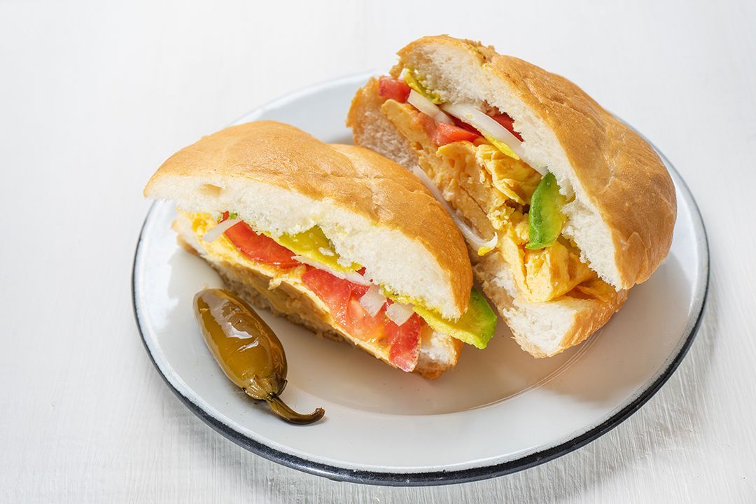 Dos sándwiches en un plato blanco con un pimiento al lado.