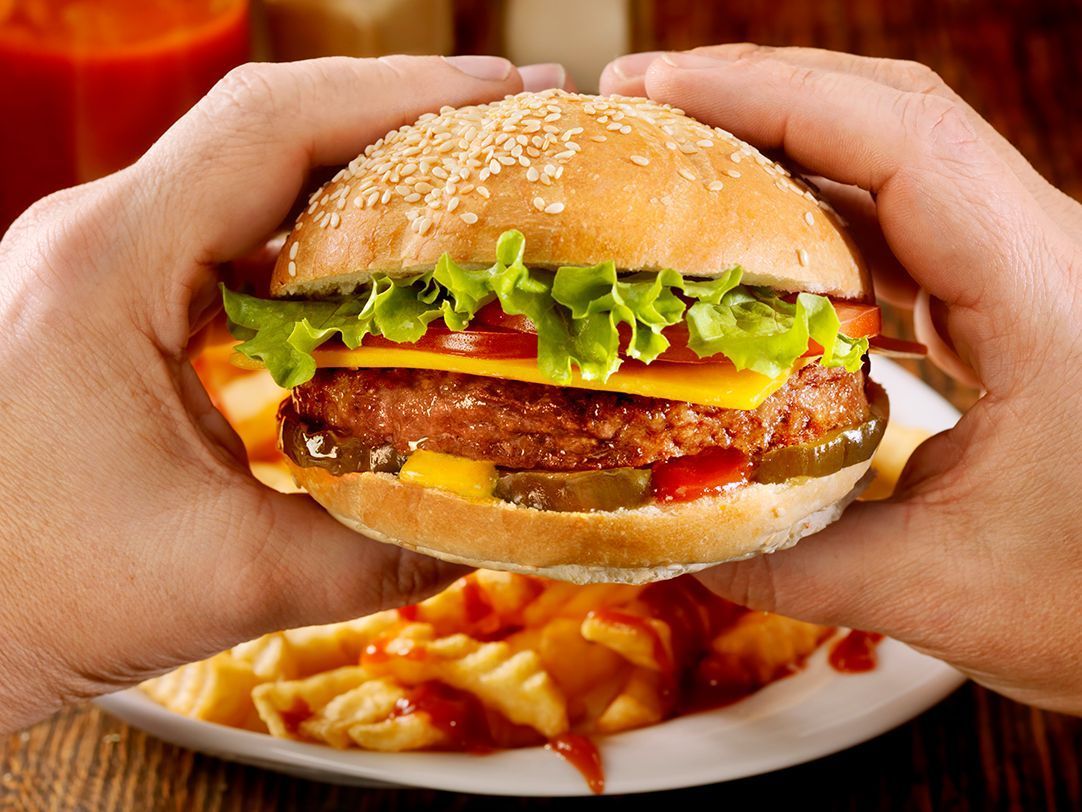 Una persona sostiene una hamburguesa en sus manos frente a un plato de papas fritas.