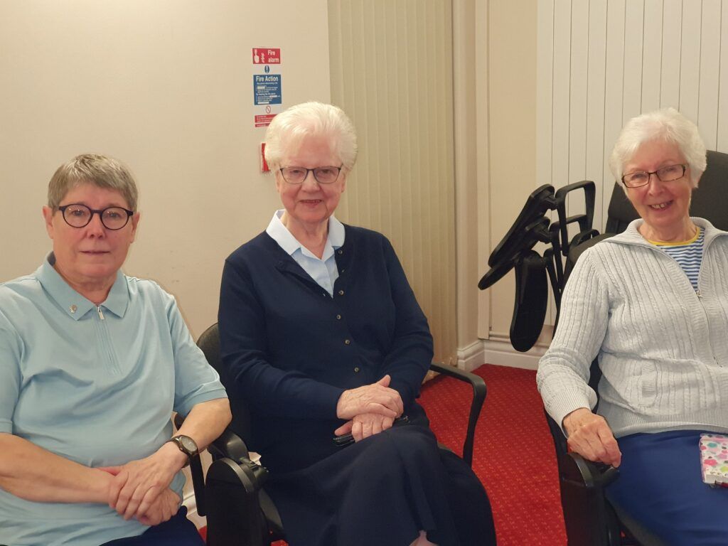 three older women are sitting in chairs and smiling for the camera .