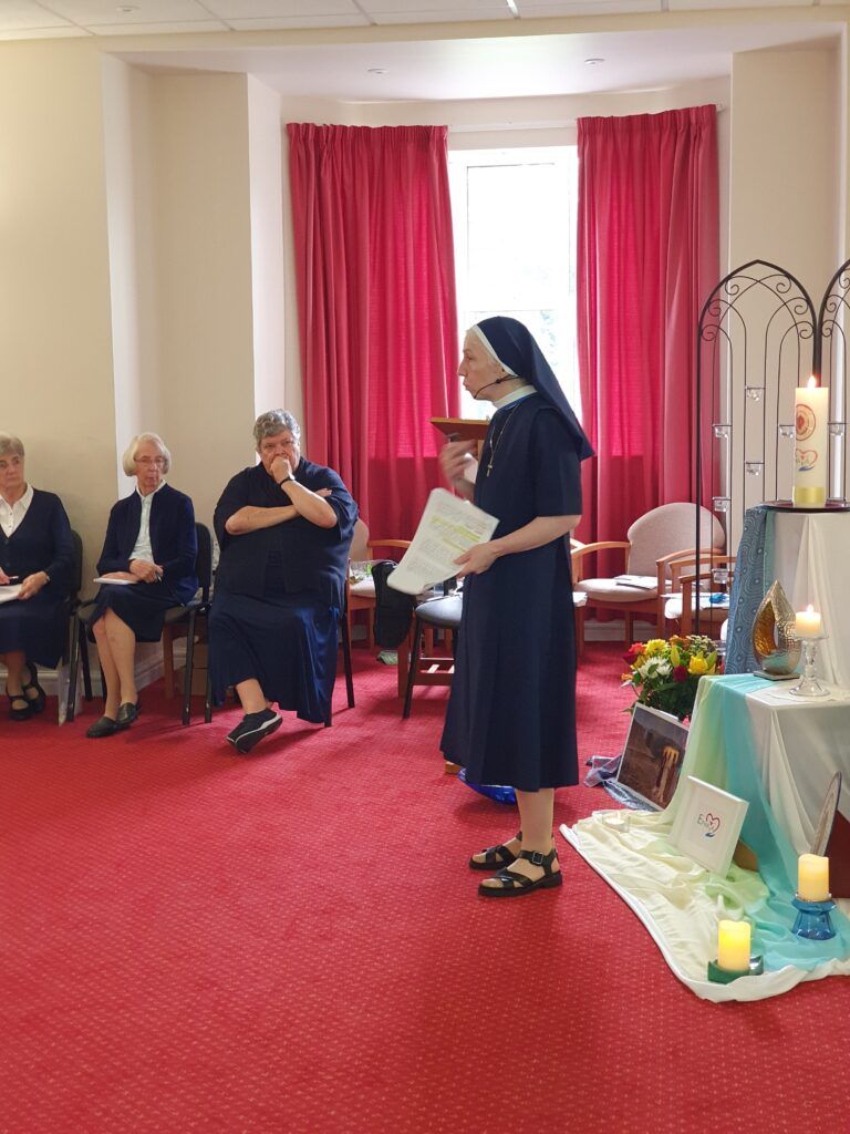 A nun is standing in front of a group of people sitting in chairs in a room.