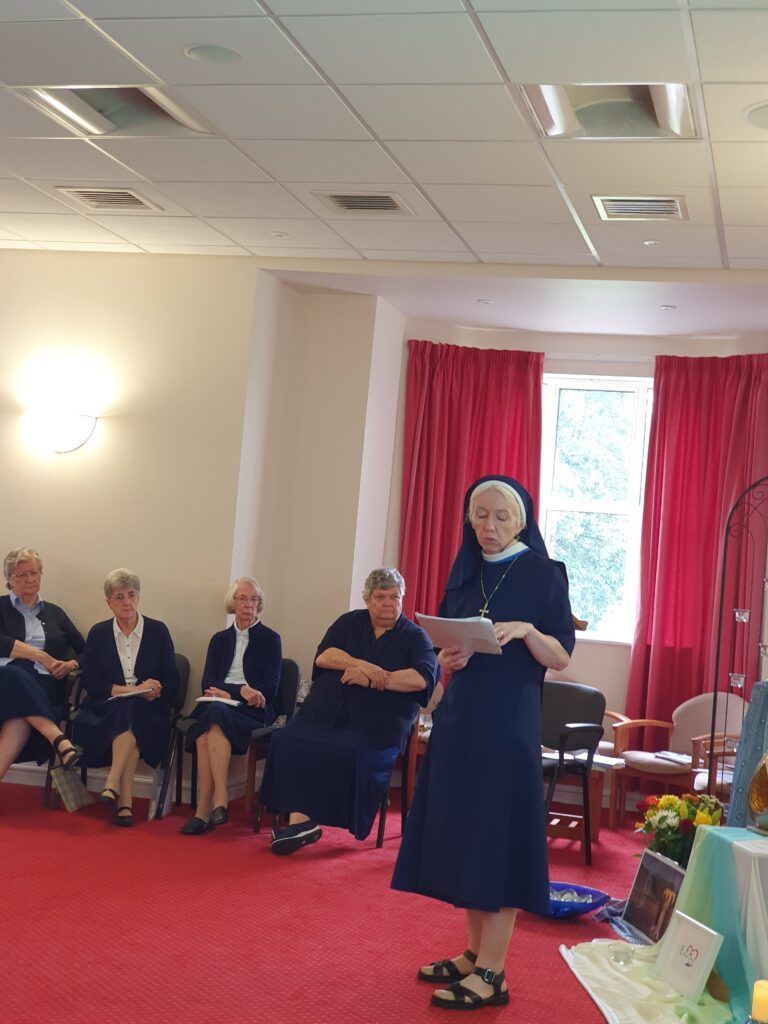 a nun is standing in front of a group of women sitting in chairs in a room .