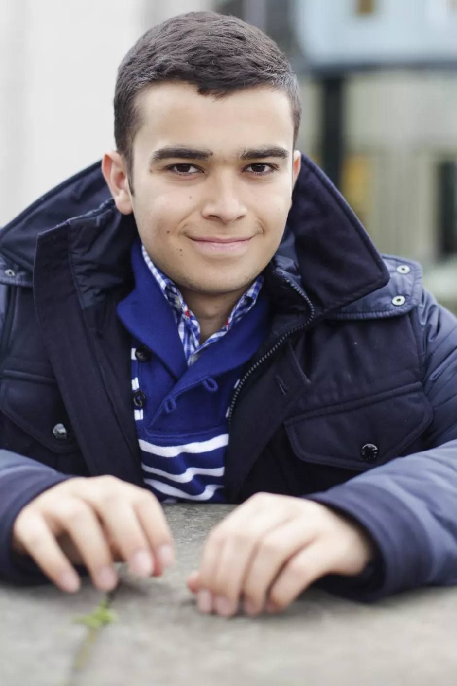 Pedro Ballester Arenas, in a blue jacket, leans on a stone surface, smiling.