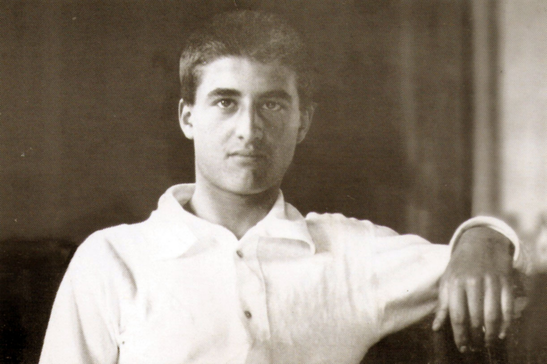 Young man in a white shirt, leaning, looking directly at the camera. Sepia-toned photo.