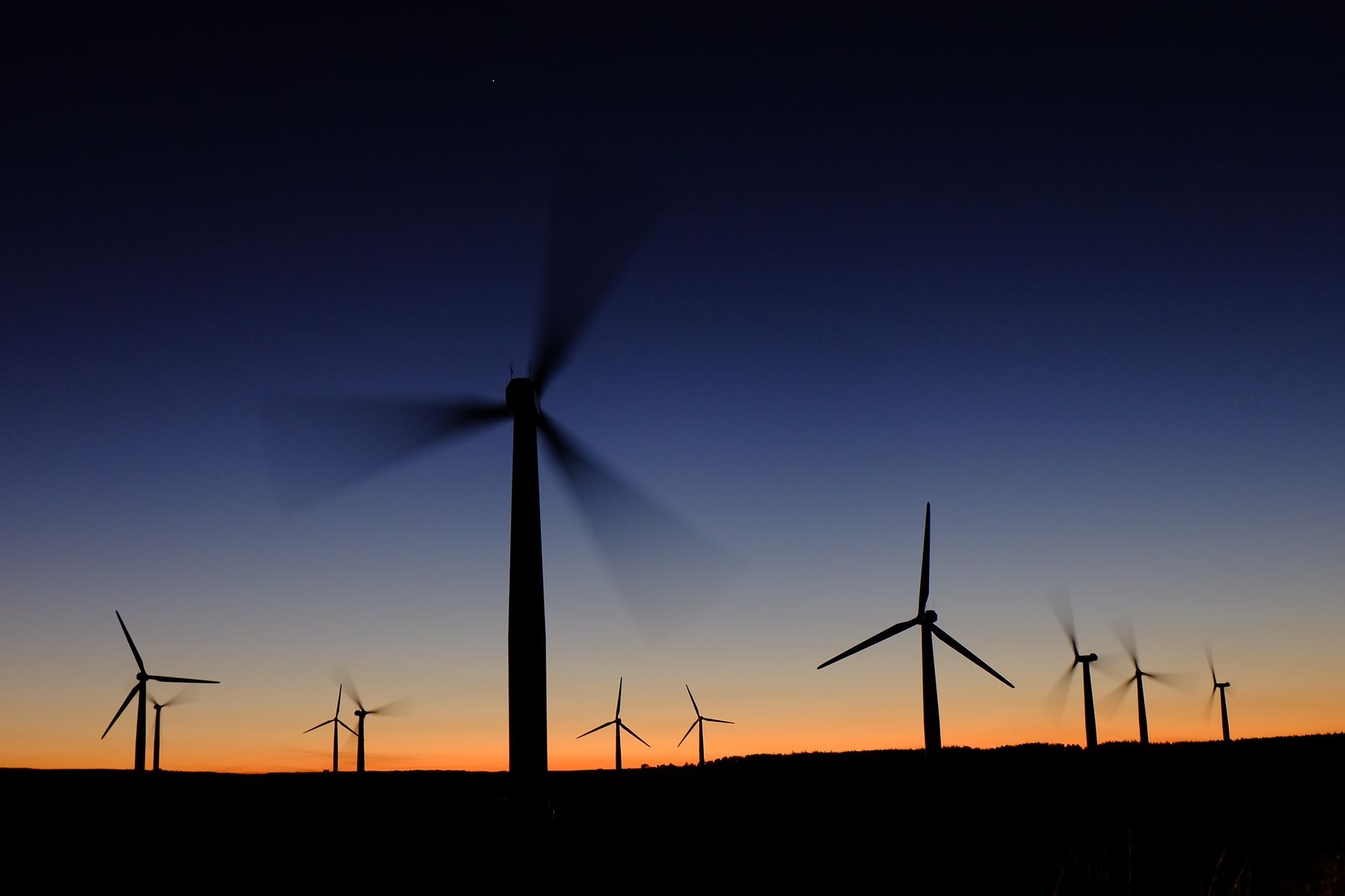 Wind turbines silhouetted against a dusky, orange and blue sky at sunset.