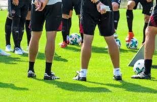 A group of soccer players are standing on a field with soccer balls.
