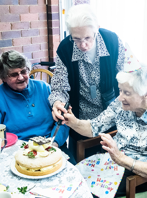 three elderly sisters are sitting at a table with a birthday cake