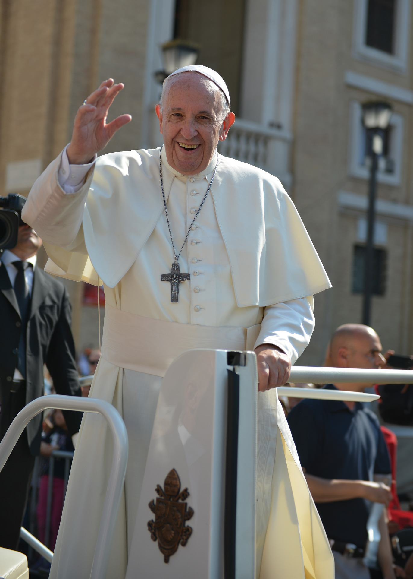 Pope Francis is standing in front of a crowd and waving.