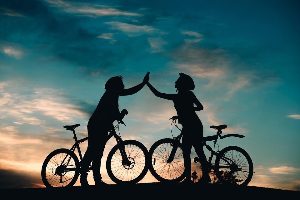 Two women are giving each other a high five while riding bicycles.