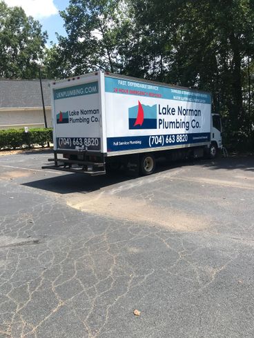 White utility trailer with Lake Norman Plumbing logo parked on asphalt under trees