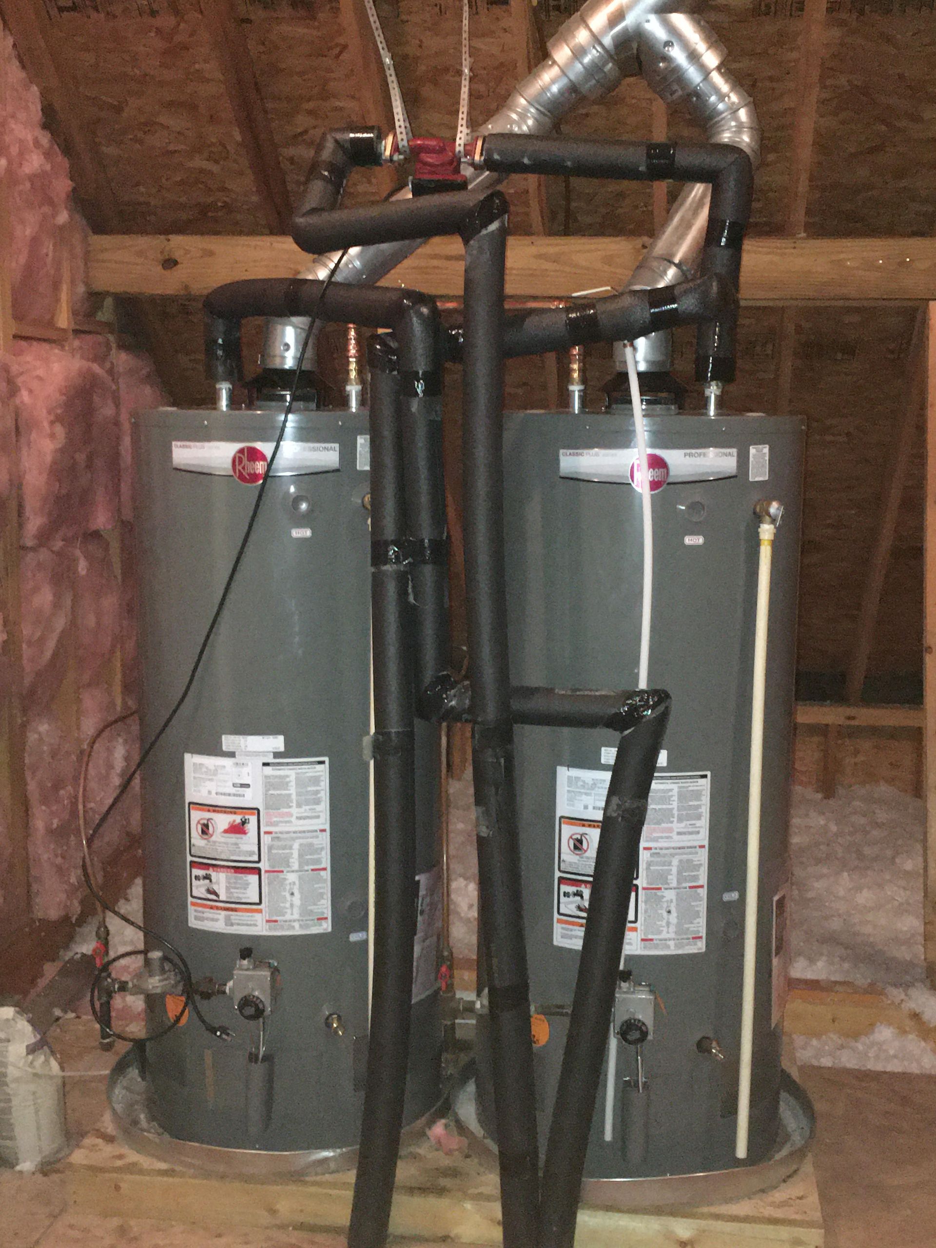 Two gray water heaters with black pipes and ductwork in an unfinished attic space