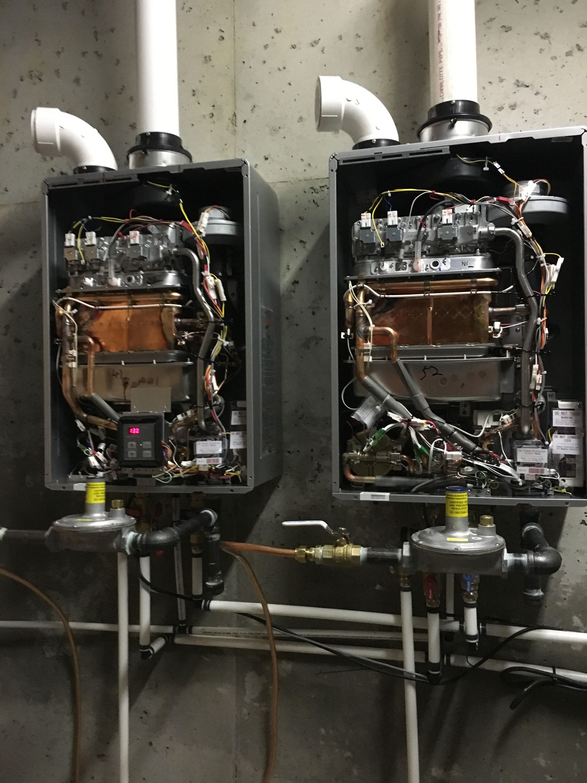 Two wall-mounted industrial boiler units with exposed pipes and vents in a utility room