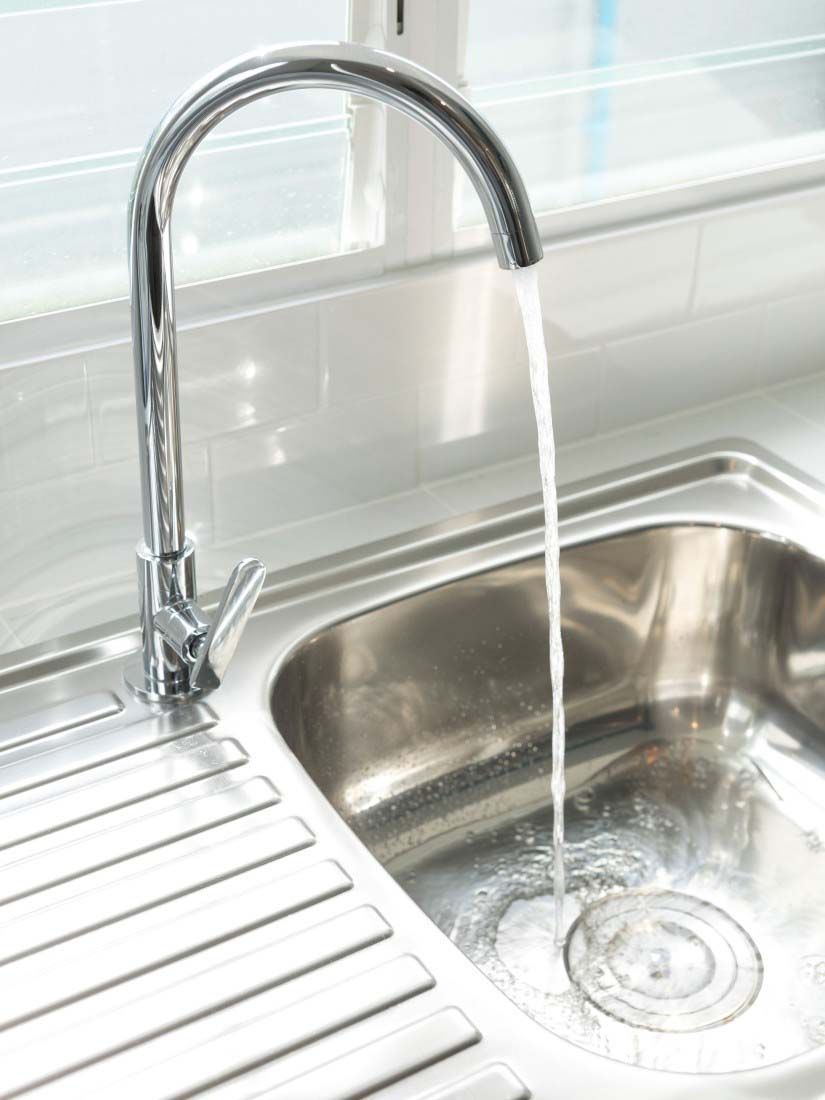 Chrome kitchen faucet running water into a stainless steel sink