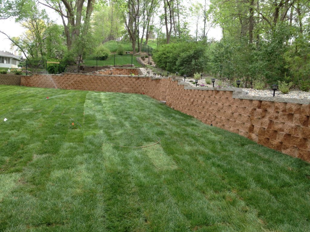 Grassy lawn with a retaining wall and trees in a landscaped backyard