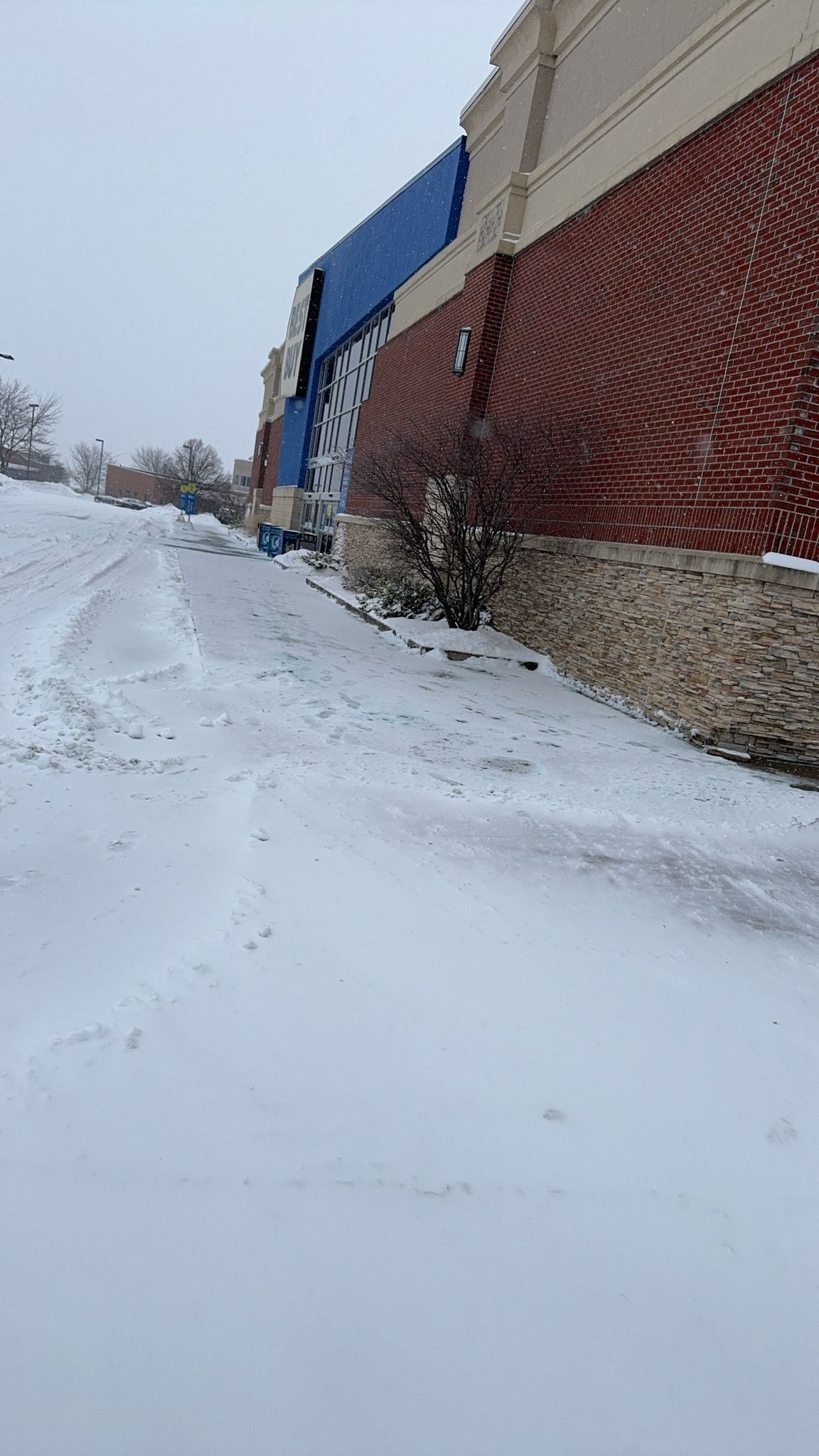 Snow-covered sidewalk beside a brick building with blue awnings on a cloudy winter day