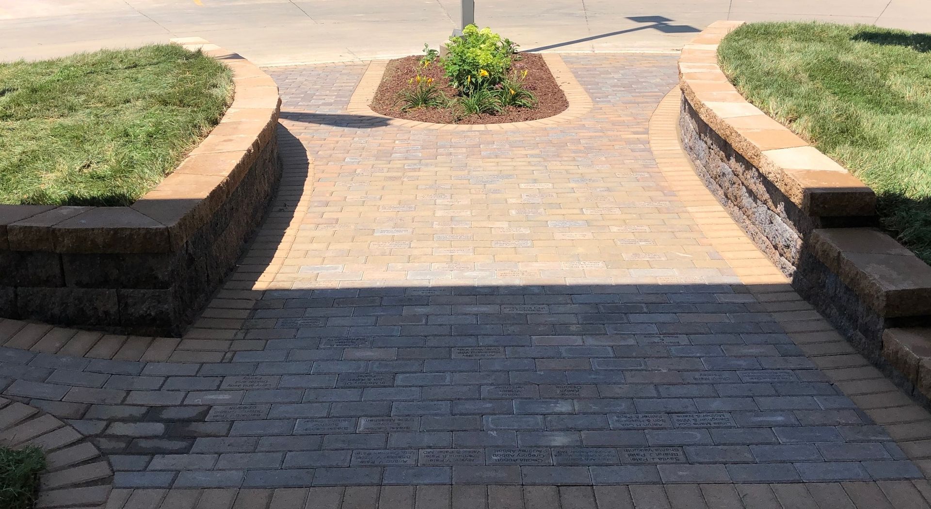 Brick walkway between raised grass planters leading to a sunlit path outdoors