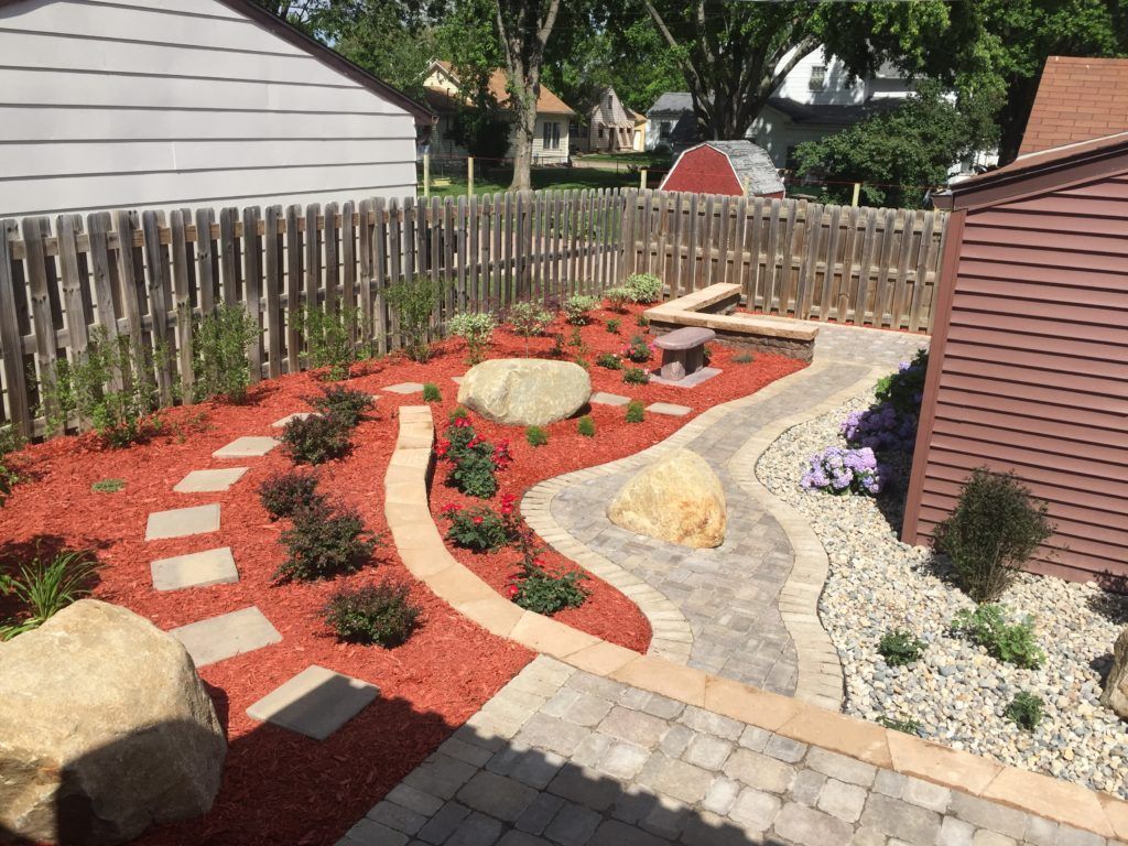 Landscaped backyard with red mulch, stone paths, large rocks, and a wooden fence