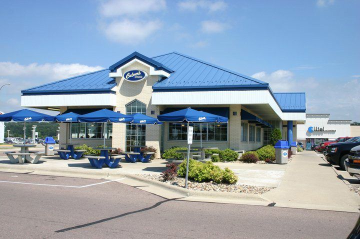 Fast-food restaurant with blue roof, outdoor patio tables, and parked cars under a clear sky
