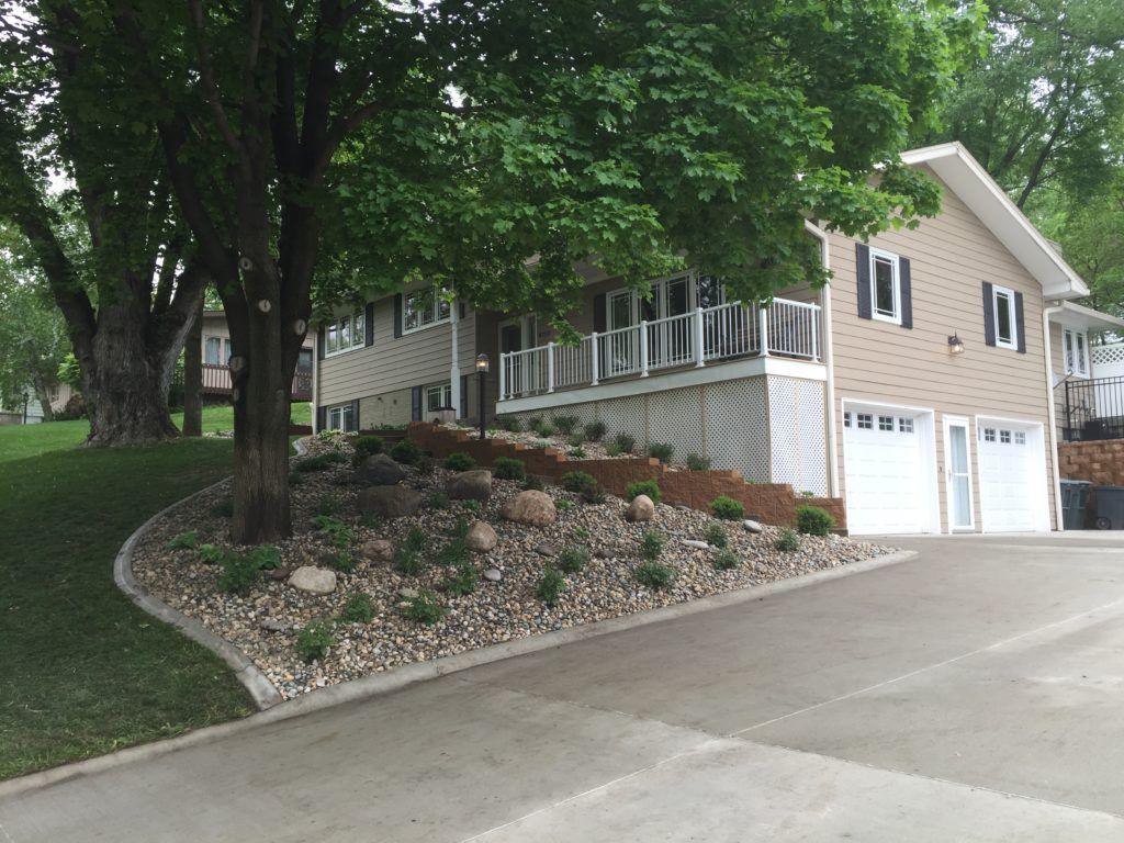 House on a sloped driveway with a stone retaining wall and trees overhead