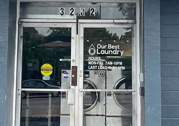 Glass storefront doors for “Our Best Laundry” with hours posted and the address 3202 above the entrance