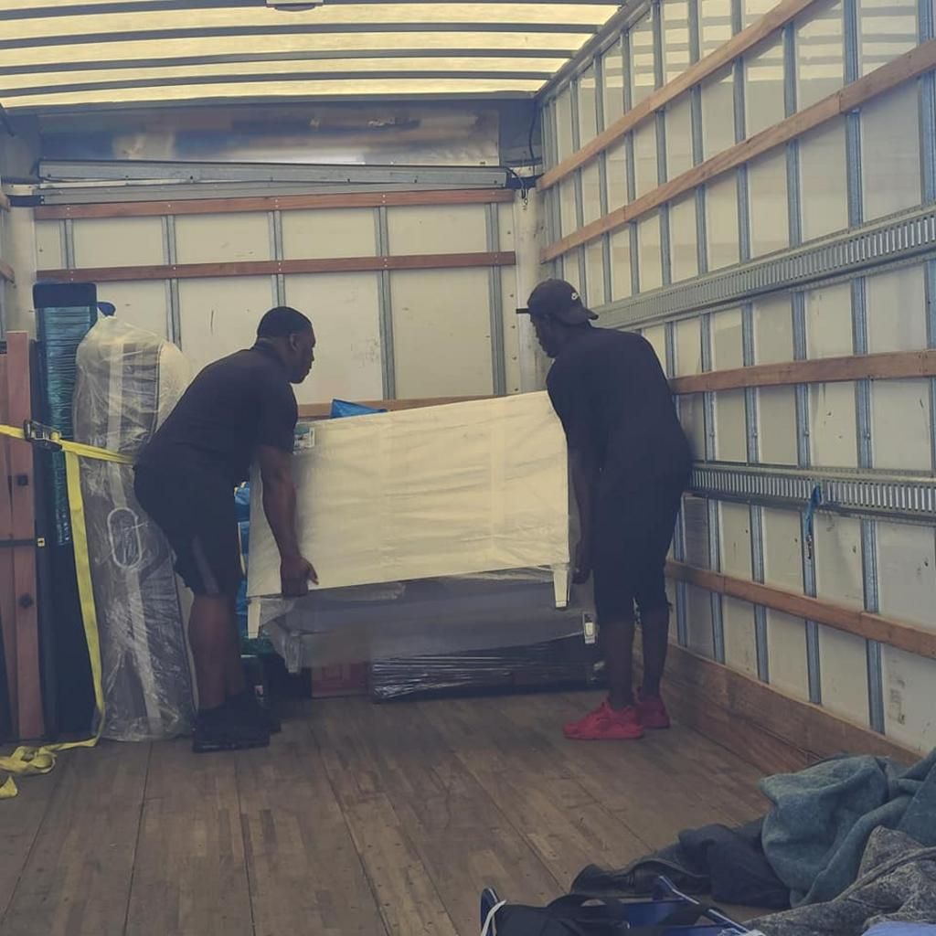 Two people loading a white sofa into a moving truck. Interior view with wooden beams and metal rails.