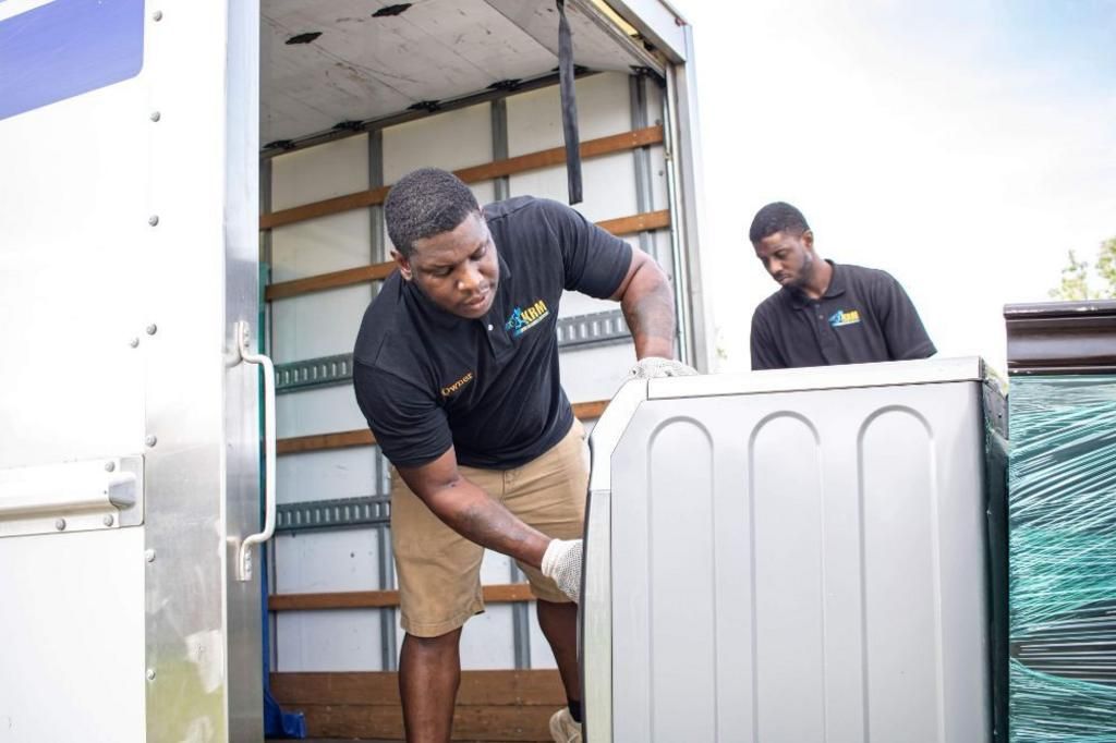 Movers loading a large, white appliance into a moving truck.