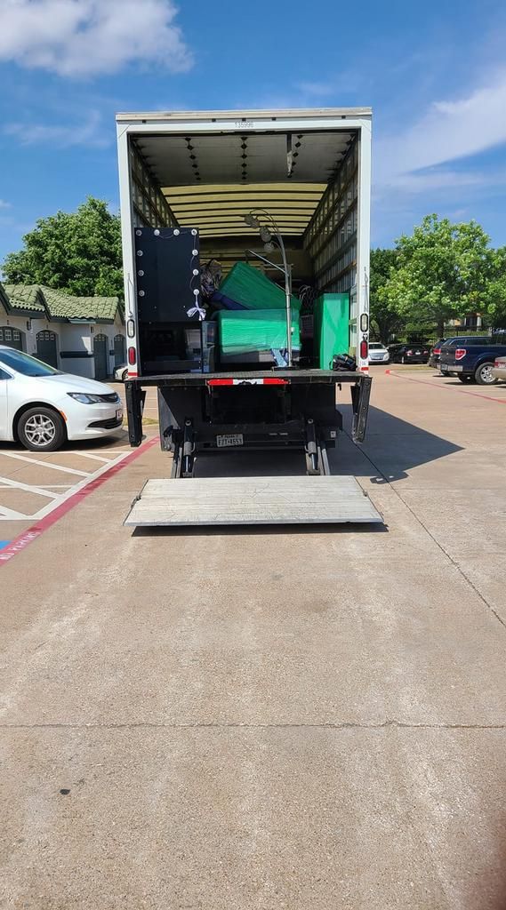 A truck with its back open, a ramp extended. Inside are machines, parked outdoors.