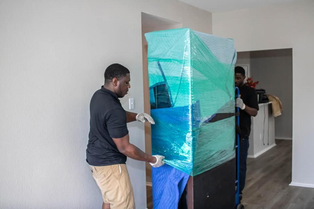 Two movers carefully maneuvering a large, wrapped item through a doorway.