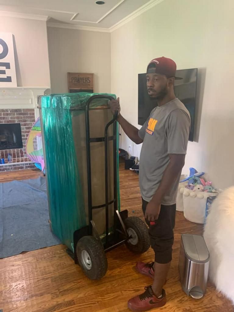 Man standing next to a wrapped box on a hand truck, indoors with fireplace and TV.