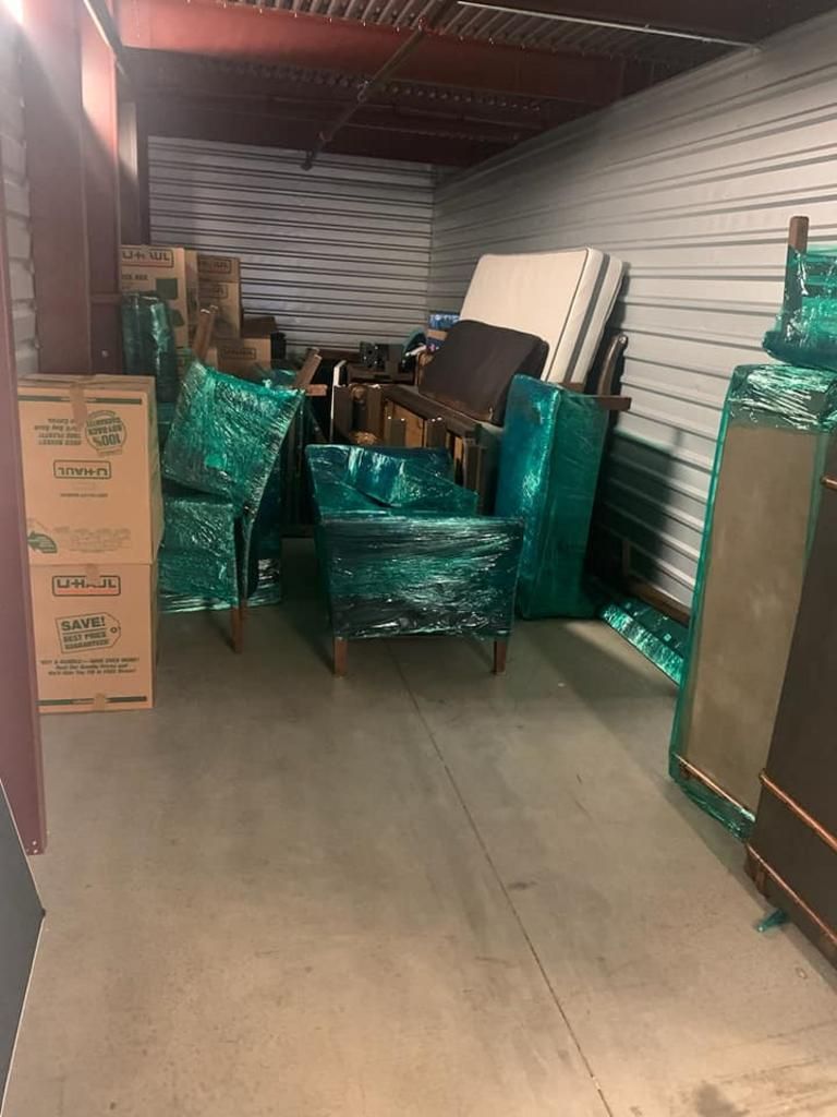 Storage unit with furniture and boxes wrapped in green plastic.