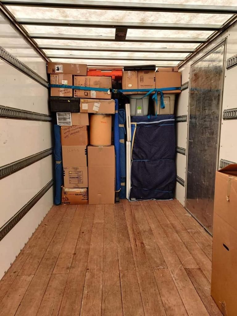 Inside a moving truck packed with cardboard boxes and furniture, secured with straps.