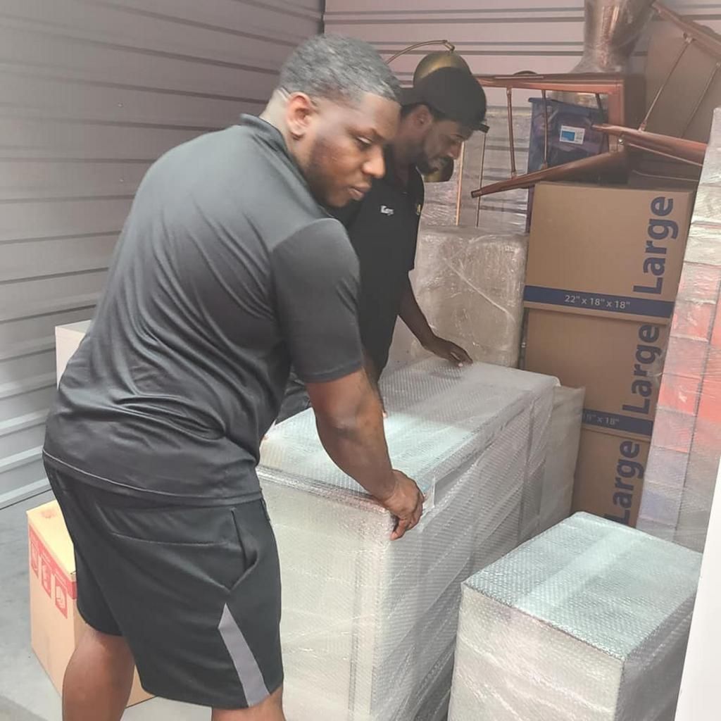 Two people loading wrapped furniture and boxes into a storage unit.