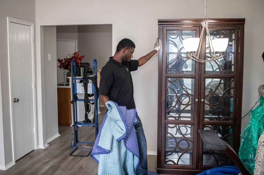 Person holding a protective pad, about to move a dark wooden cabinet, indoors.