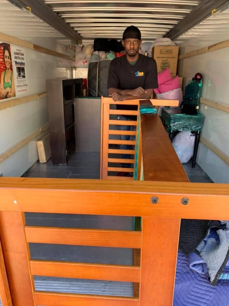 Person standing in a moving truck, surrounded by furniture and packed items.