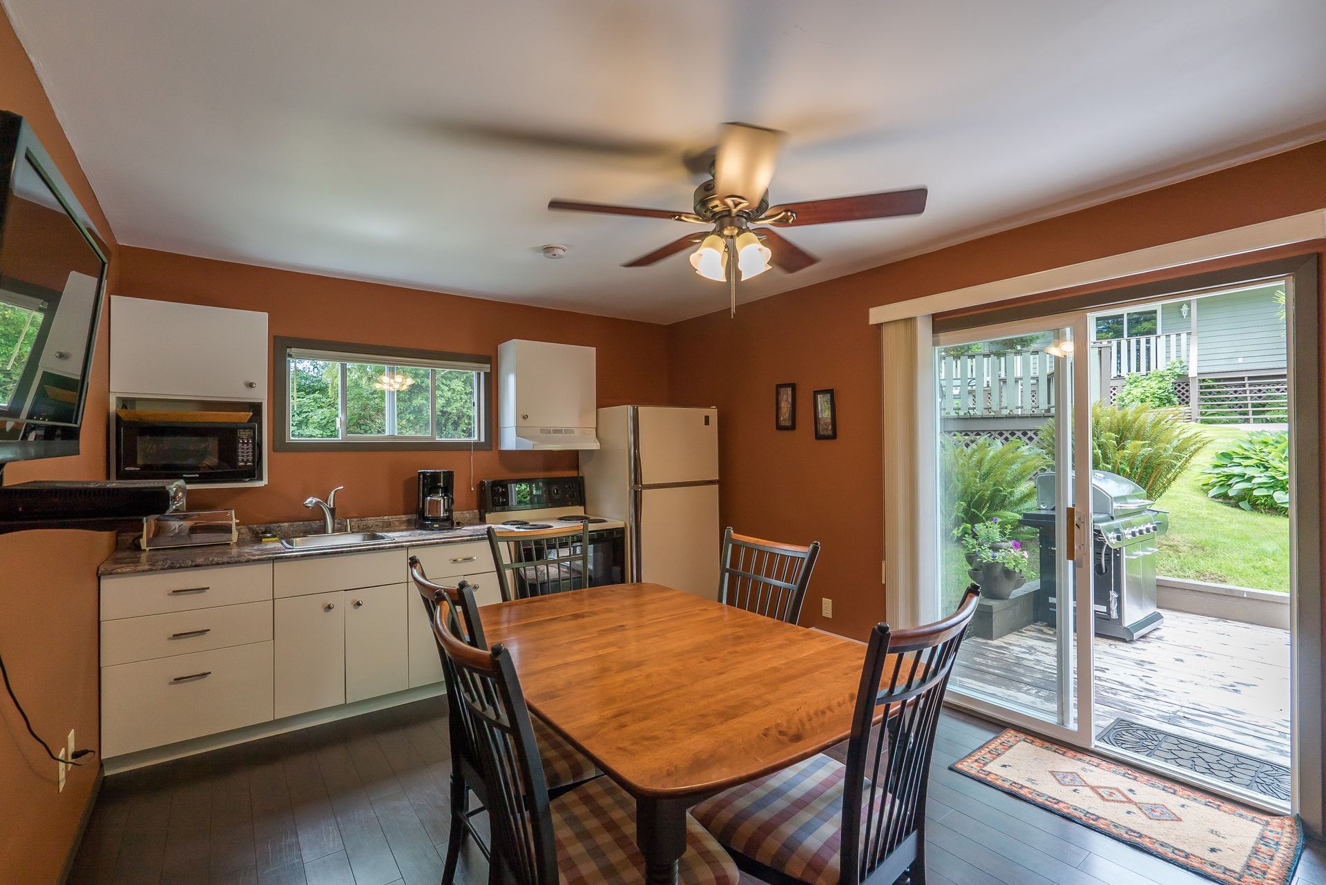 A cozy kitchen and dining area with rust-colored walls, light wood cabinets, a wooden table, and a glass patio door.