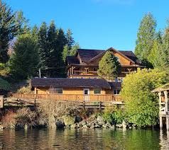 A wooden lakeside lodge set against a backdrop of green pine trees under a clear blue sky.