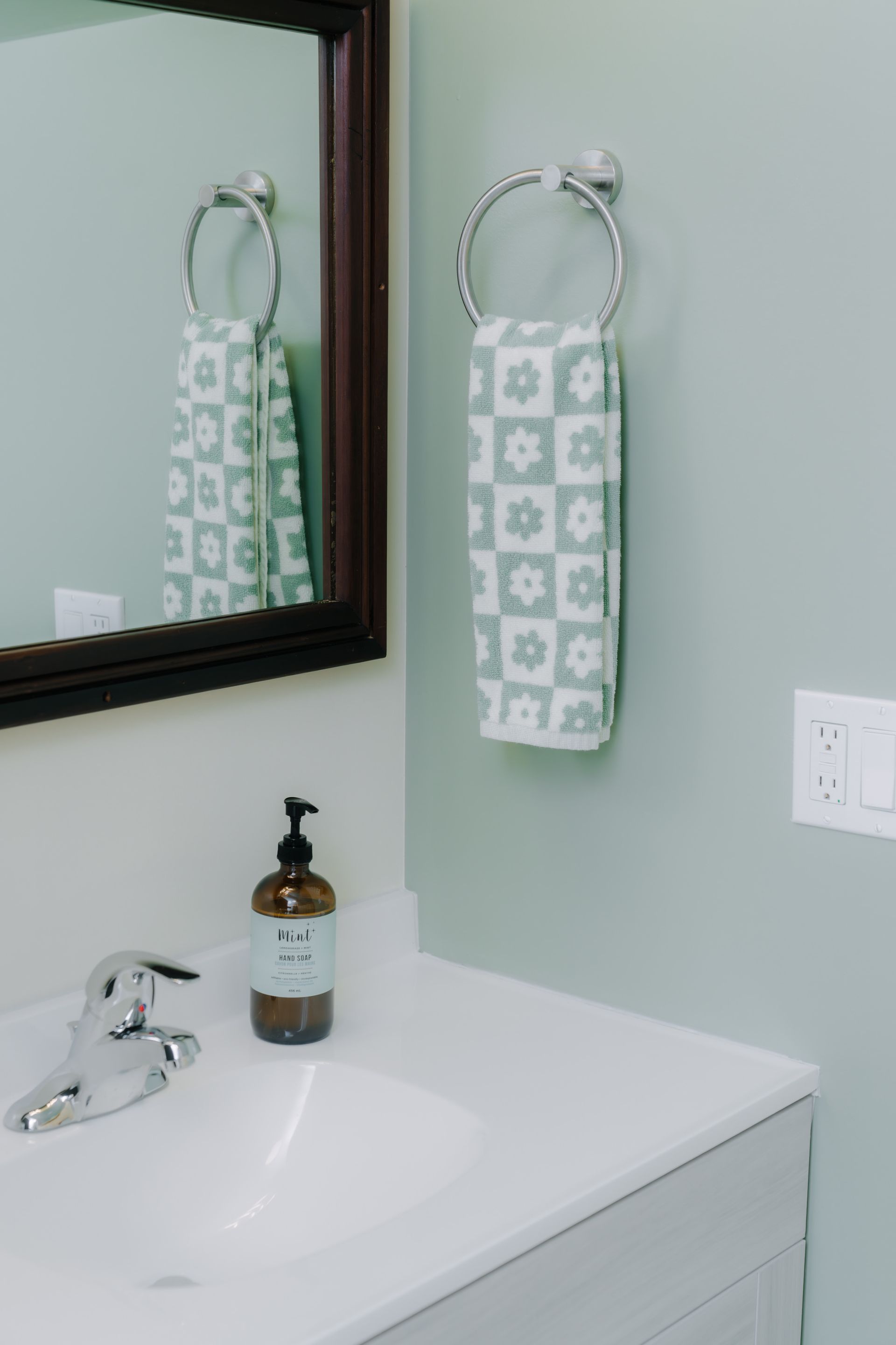 A bathroom vanity with a white sink, faucet, soap dispenser, and a green-and-white patterned towel hanging on a ring.