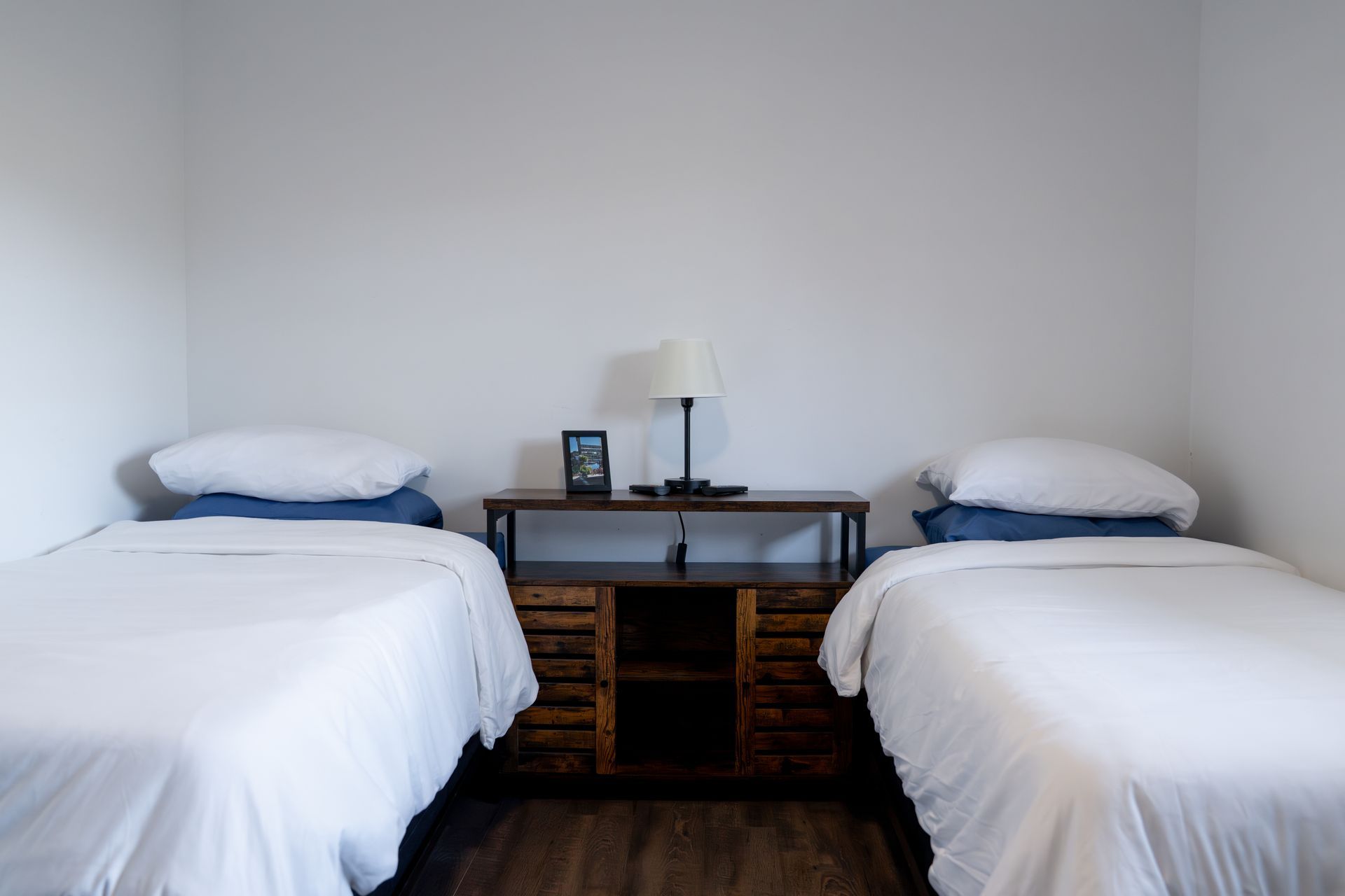 Two twin beds with white linens and blue pillows, separated by a dark wood nightstand with a lamp.