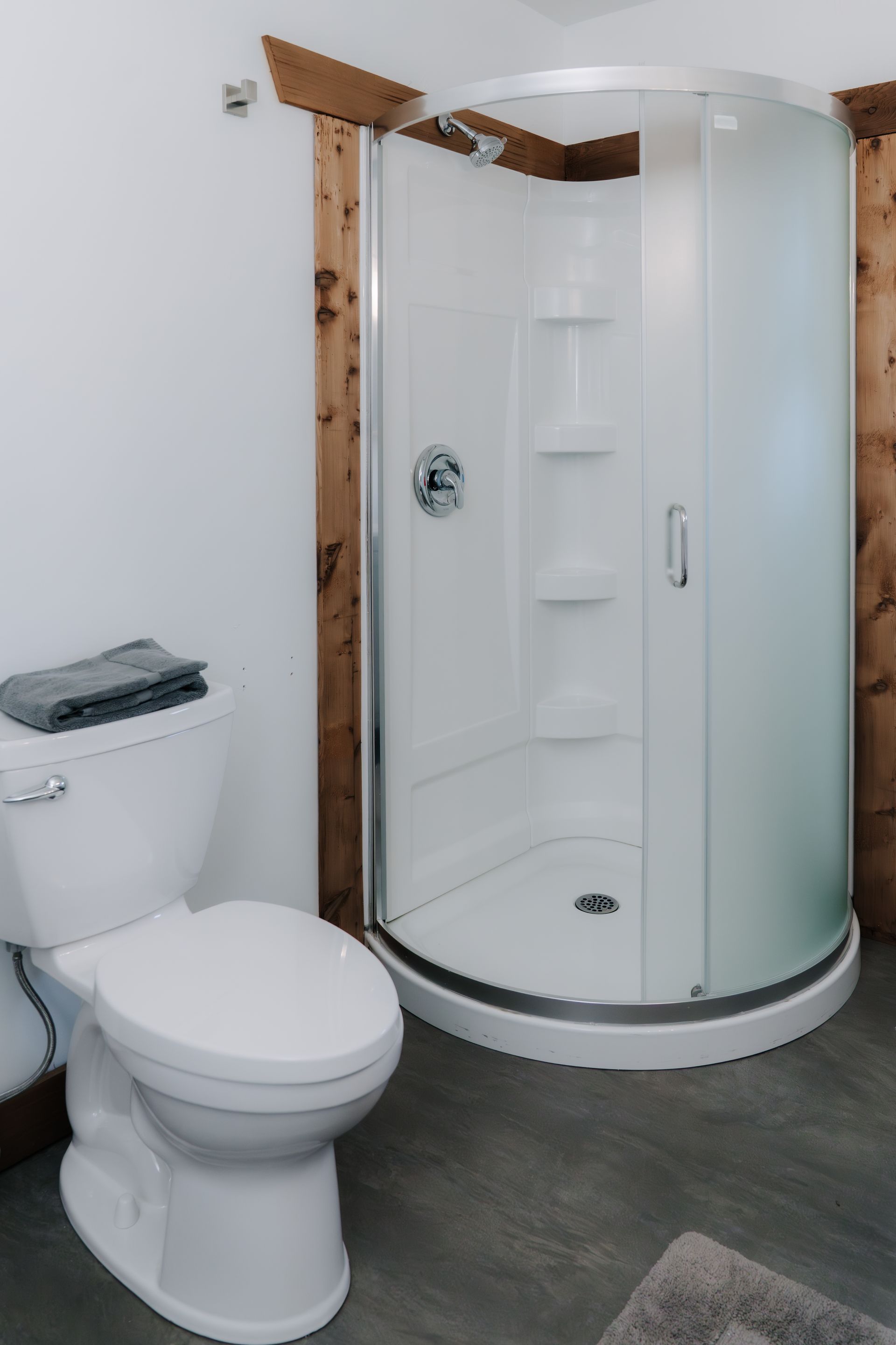 A white toilet next to a corner shower stall with frosted glass doors, set against white walls and wooden trim.