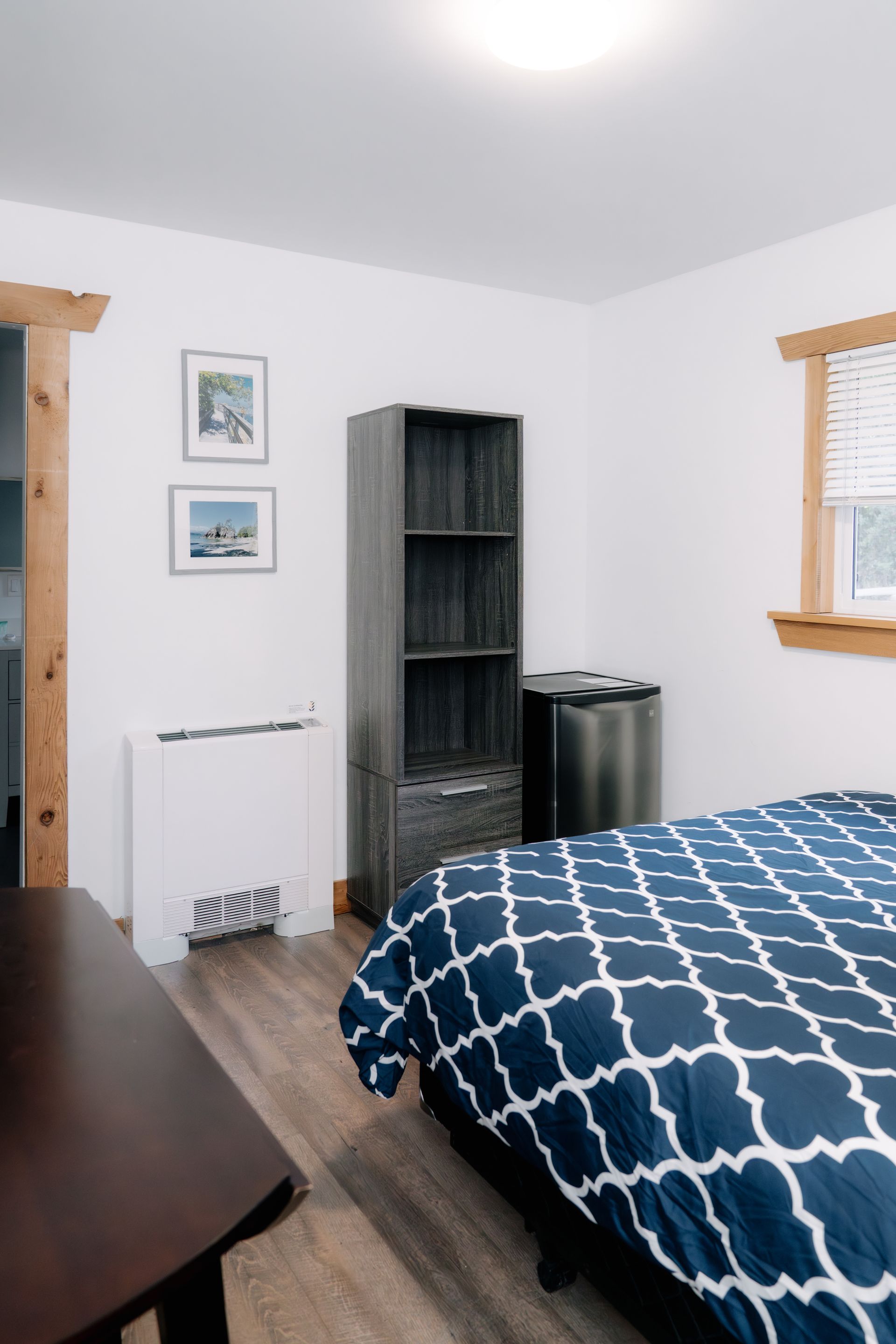 A bedroom with a blue patterned comforter, wooden trim, a grey shelf, and a white wall heater.