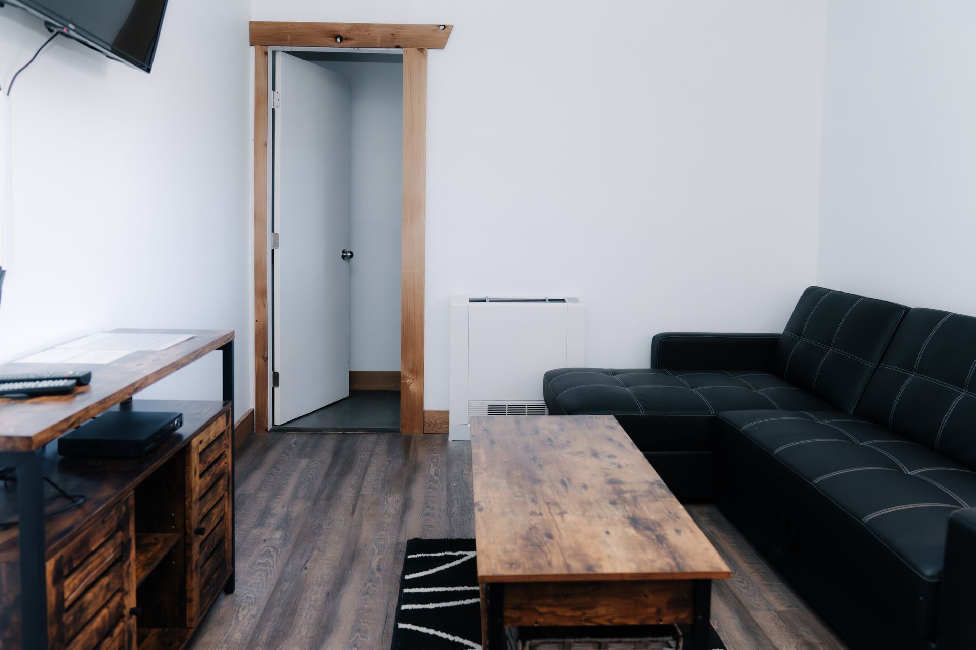 A modern living room with a black sectional sofa, a wooden coffee table, a wooden media console, and an open doorway.