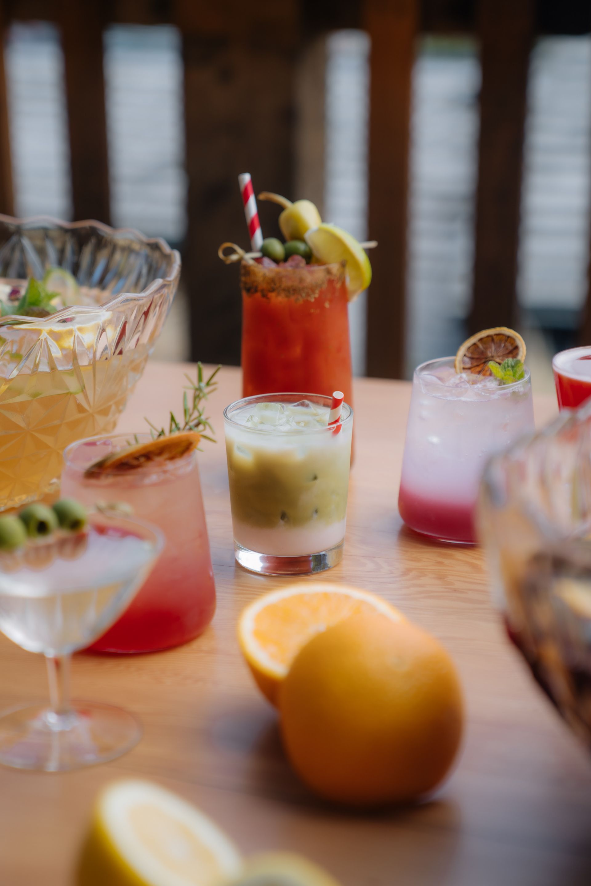 A spread of various colorful cocktails and bowls of punch on a wooden table with fresh oranges in the foreground.