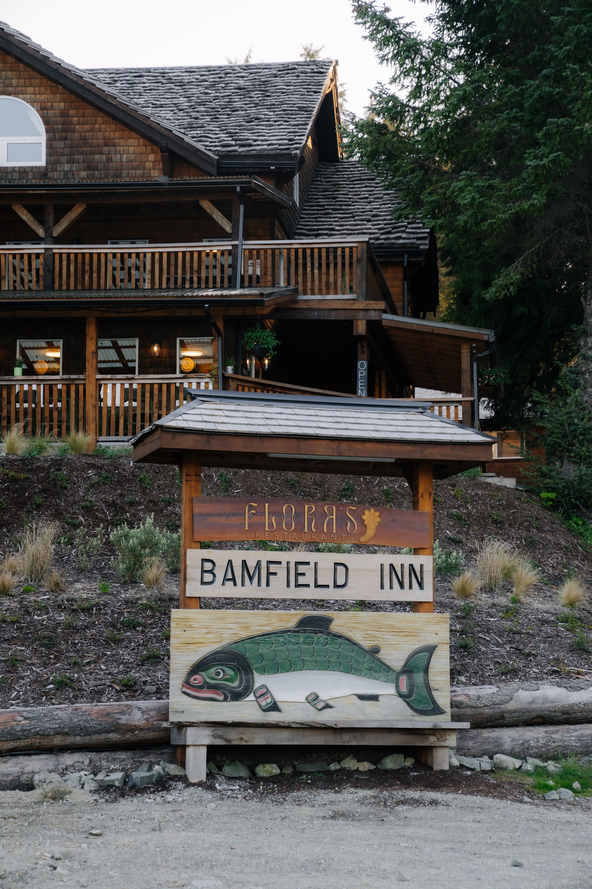 A house sits atop a grassy embankment above a water-front bulkhead, connected to a floating dock by a wooden ramp.