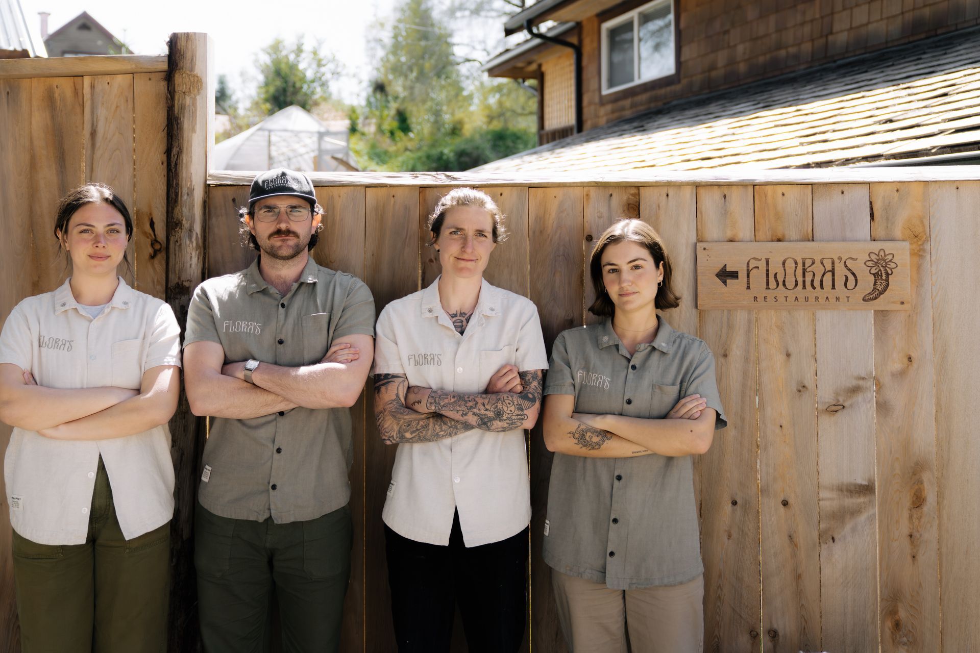 Four people wearing matching shirts stand with their arms crossed in front of a wooden fence with a sign for Flora's.