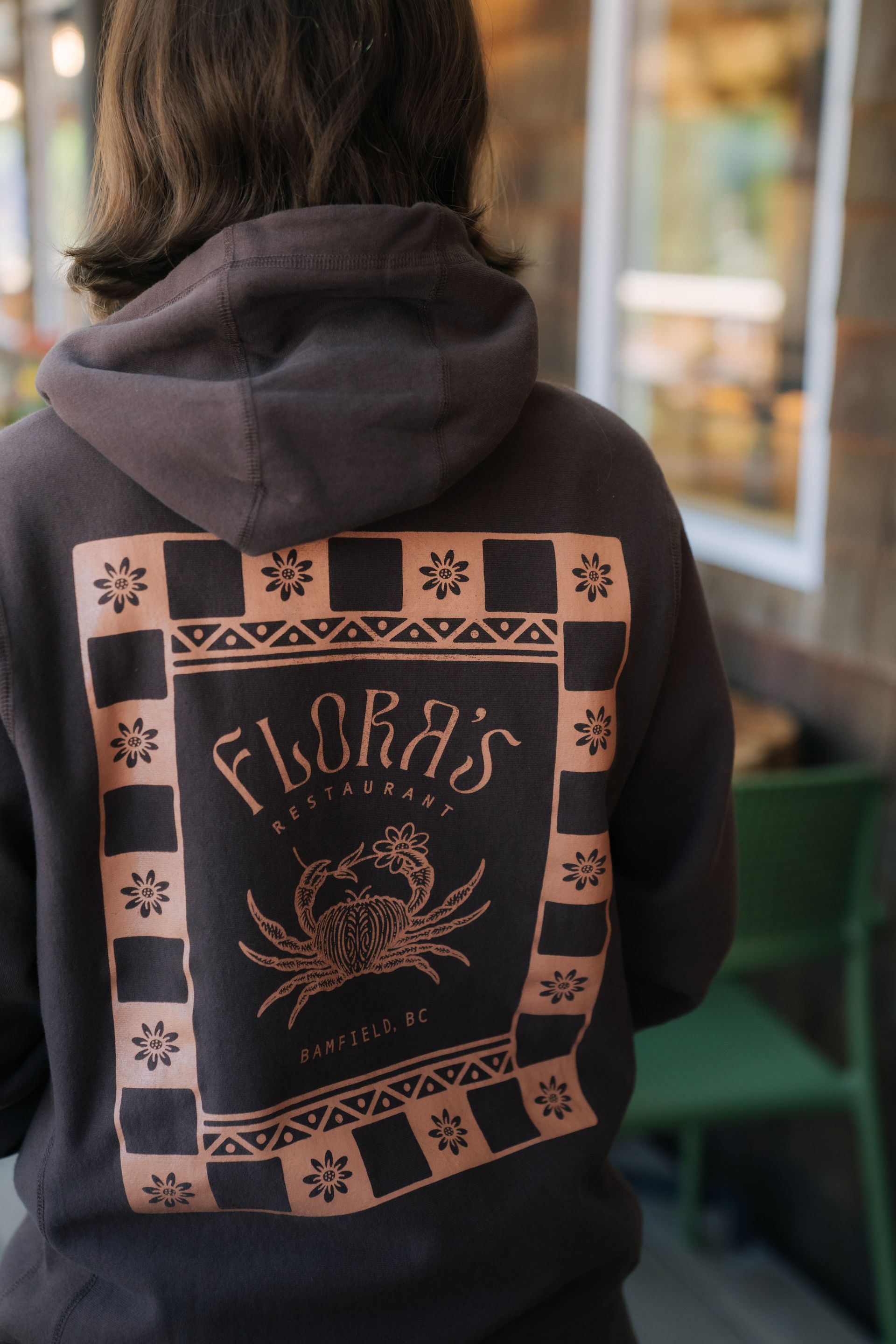 A person wearing a brown hoodie with a graphic on the back featuring 